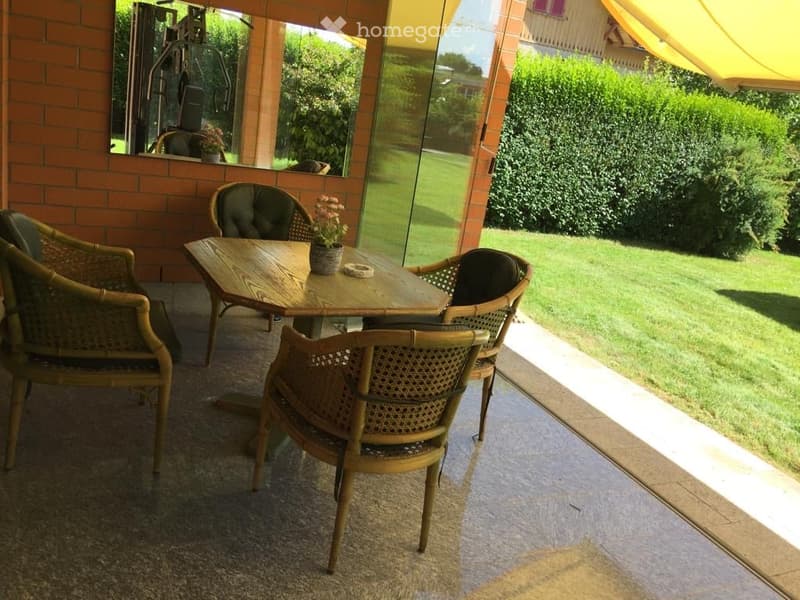 wooden table, wicker chairs, green lawn, brick wall, yellow awning, glass door, flowers