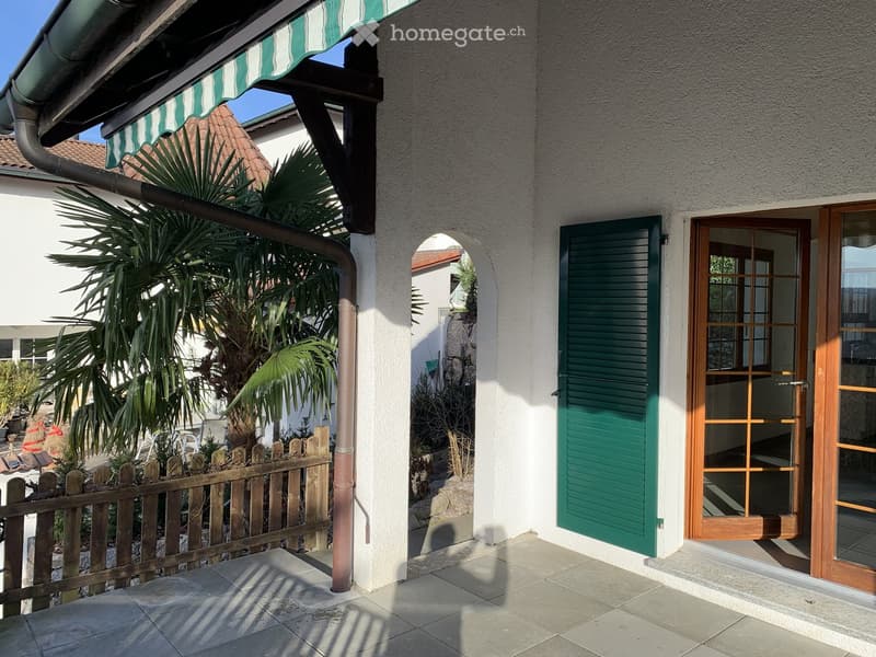 Balcony area with tiled flooring, green shutters, wooden fence, and palm trees in the background.