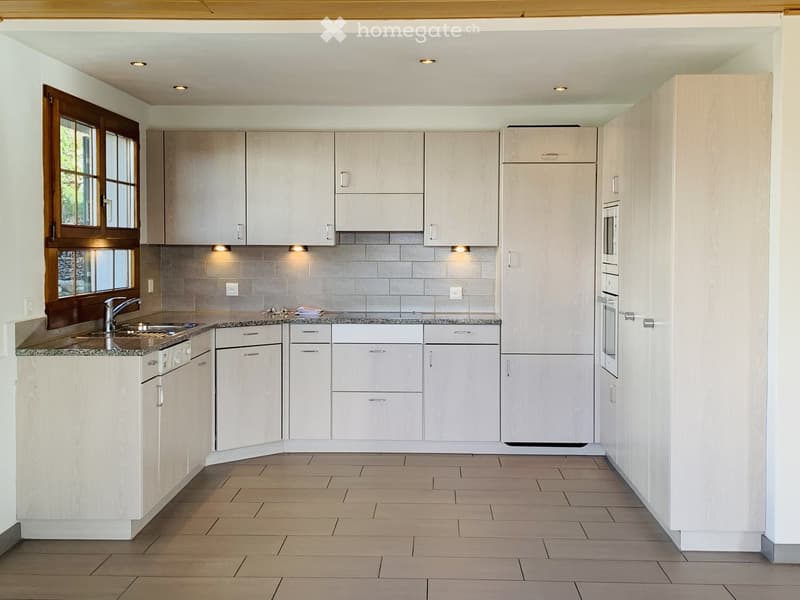 Modern kitchen with light-colored cabinets, granite countertops, and built-in appliances including a sink, oven, and microwave. Features recessed lighting and a large window with wooden frame.