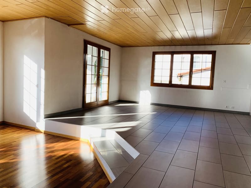 Empty room with wooden and tiled flooring, large windows, and a sliding glass door leading outside.