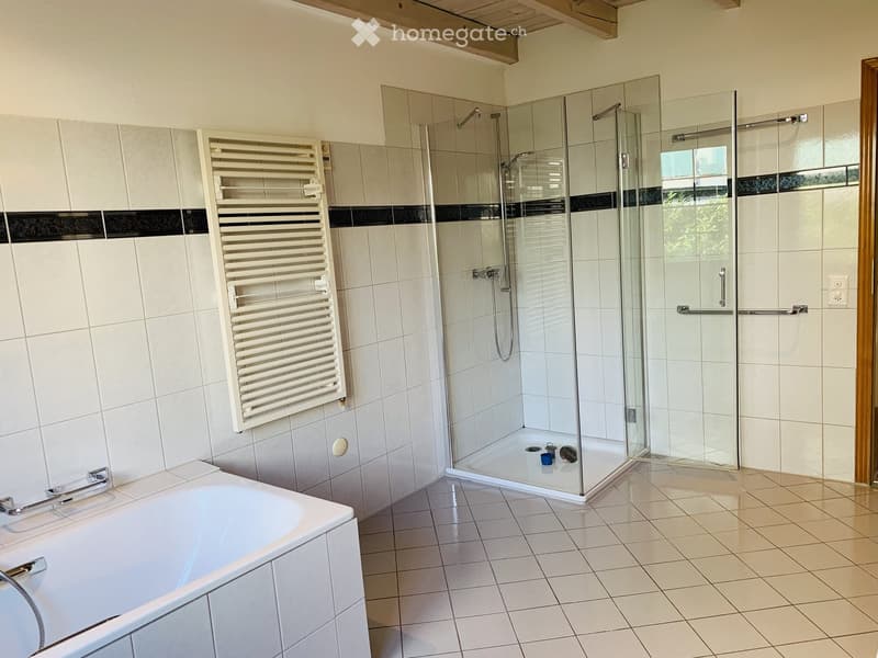 Modern bathroom with a bathtub, glass-enclosed shower, and a white radiator. The walls are tiled with a black accent border, and the floor is tiled in light beige.