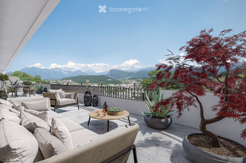 A spacious balcony with a panoramic mountain view, featuring a large sectional sofa, a coffee table, decorative lanterns, and potted plants including a bonsai tree and a large aloe vera plant.