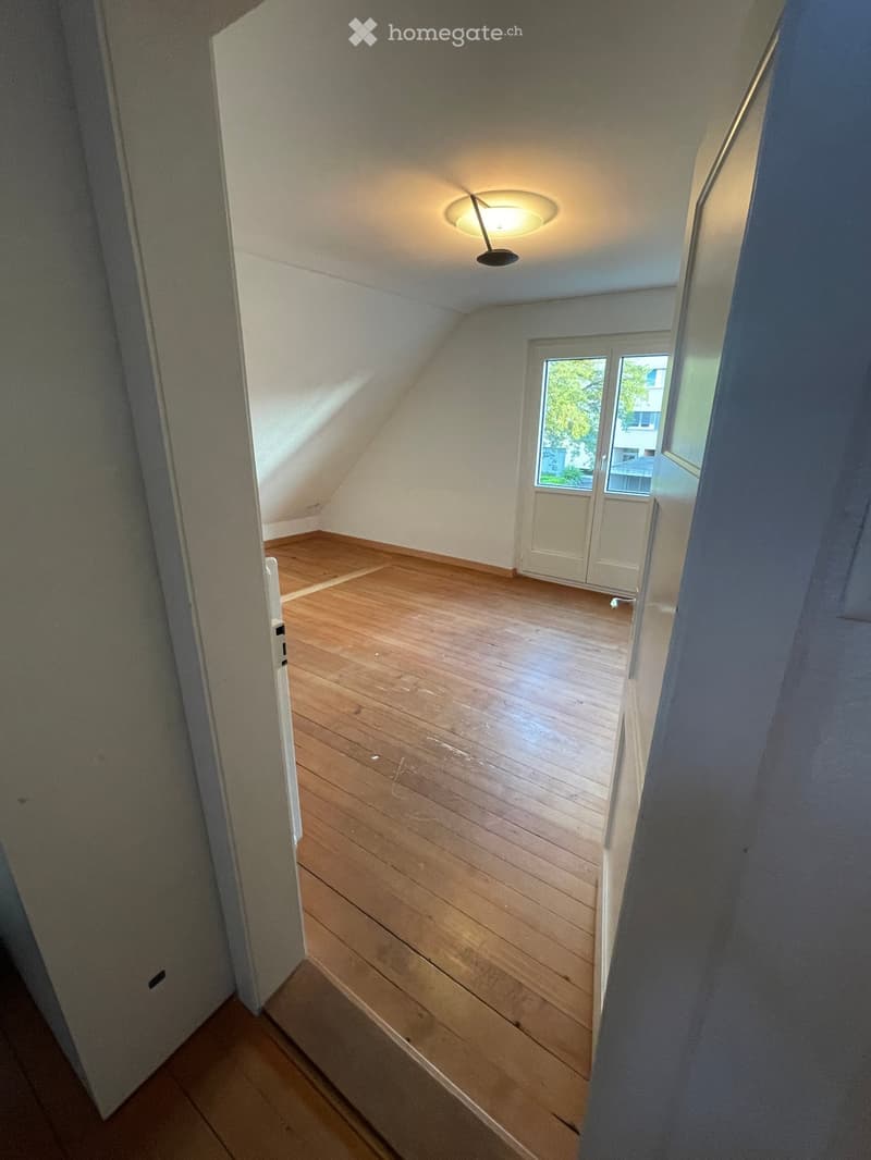 Empty attic room with wooden flooring, white walls, and a skylight window. No furniture or equipment present.