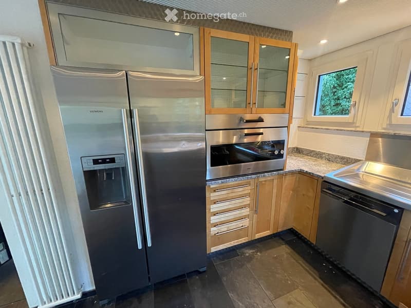 Modern kitchen with stainless steel appliances, including a refrigerator, oven, and dishwasher, complemented by light wood cabinets and granite countertops.