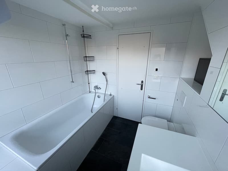 Modern bathroom with white tiles, a bathtub, toilet, mirror, and shower fixtures.