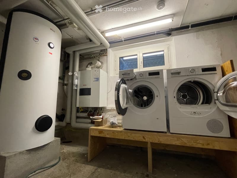 Utility room with a washing machine, dryer, water heater, and a small wooden table holding miscellaneous items.