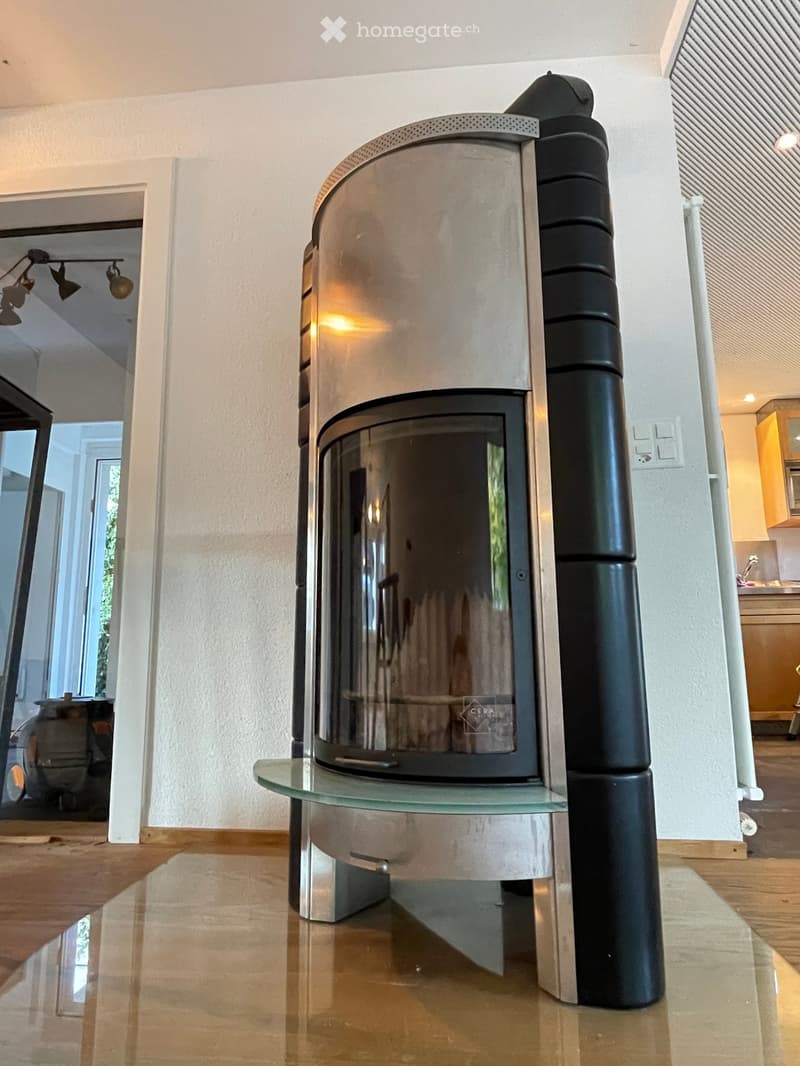 Modern, sleek fireplace with glass front and glass shelf, placed on polished wooden floor.
