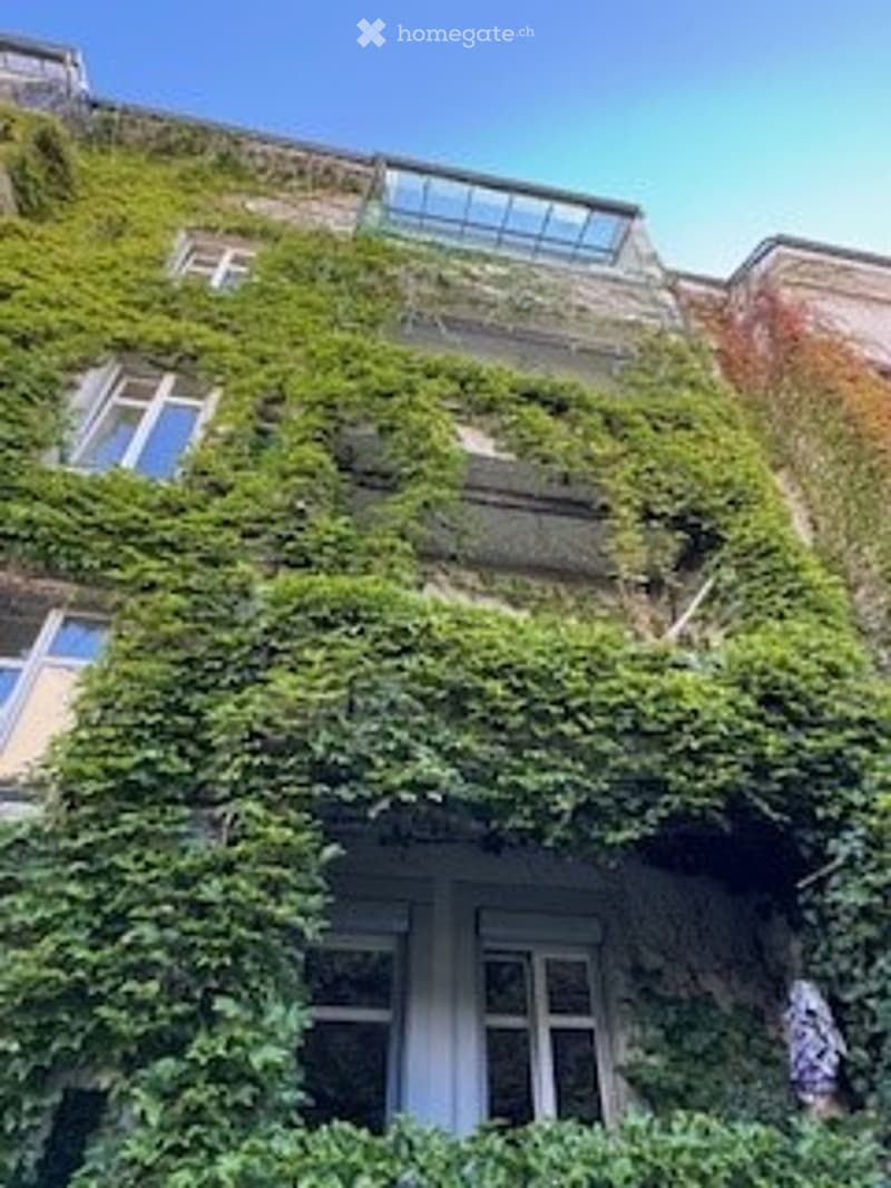 Multi-story building with ivy-covered facade, large windows, and a glass roof section on the top floor.