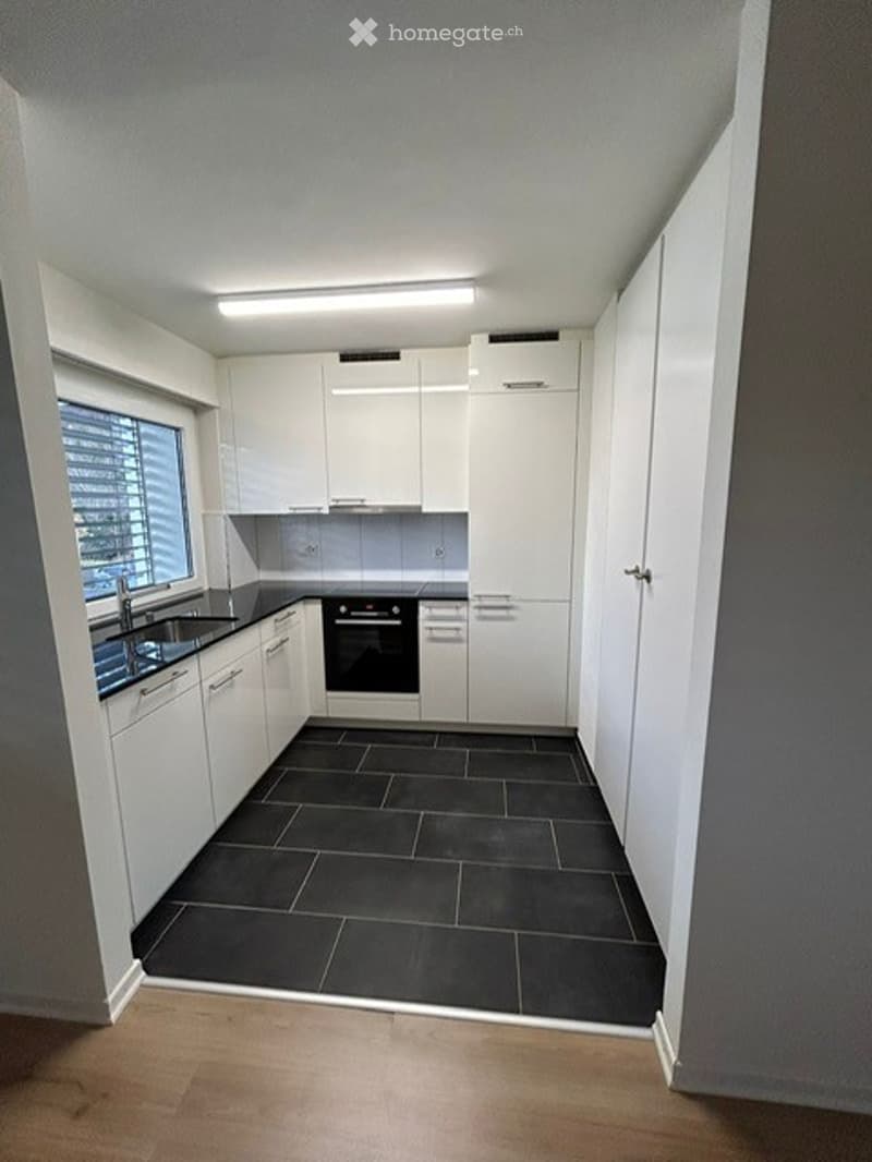 Modern kitchen with white cabinets, black tiled floor, and stainless steel appliances including a sink and oven.