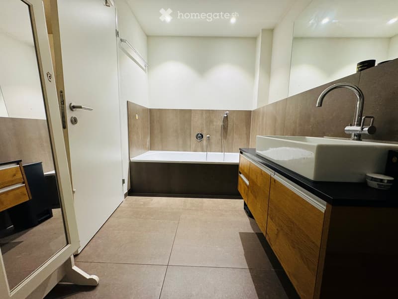 Modern bathroom with a white bathtub, a white sink with a modern faucet, wooden cabinets, and a tiled floor.