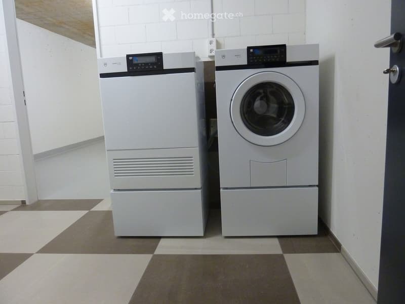 A small room with a washing machine and dryer stacked side by side, white brick walls, and a checkered floor.