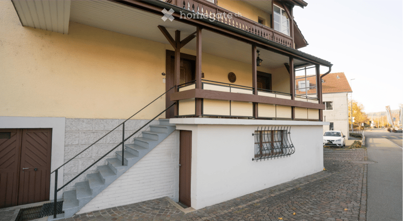 Two-story residential building with a balcony, wooden railings, and a staircase leading to the entrance.