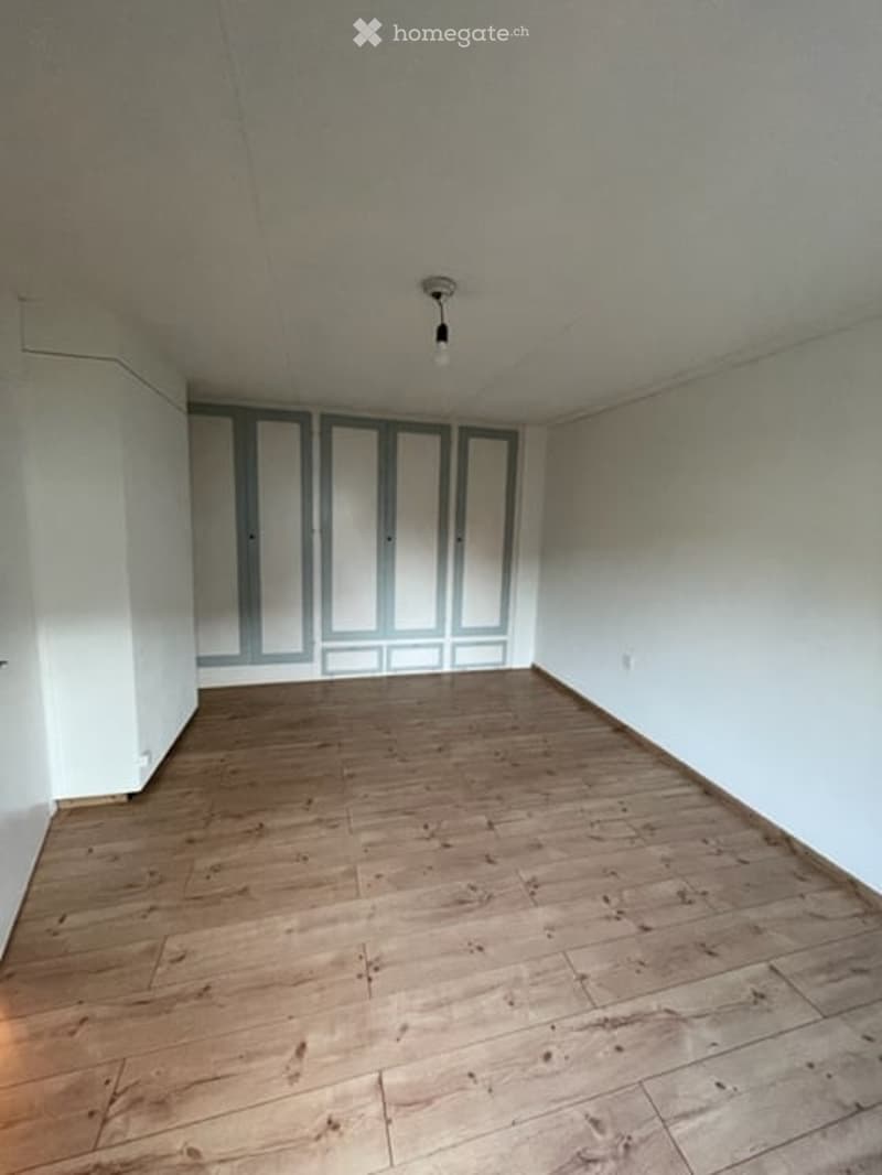 Empty room with wooden flooring, white walls, and built-in closet with mirrored doors.
