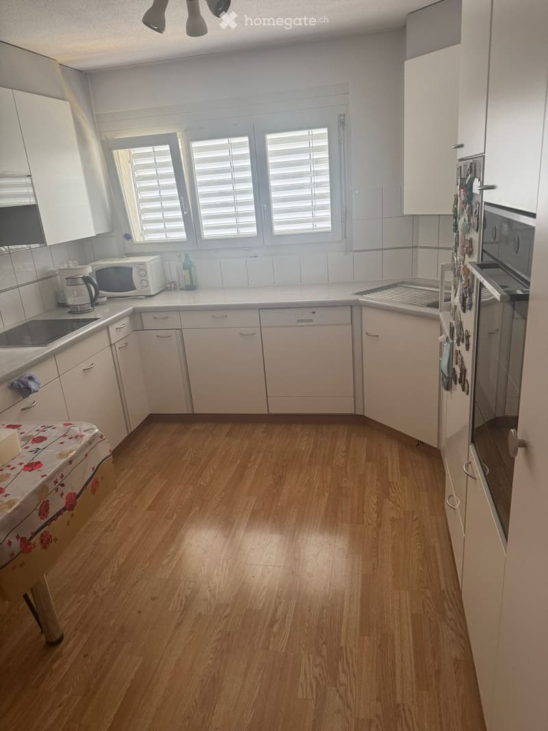 Modern kitchen with light-colored cabinets, wooden flooring, and stainless steel appliances including a microwave, electric kettle, refrigerator, oven, sink, and dishwasher.