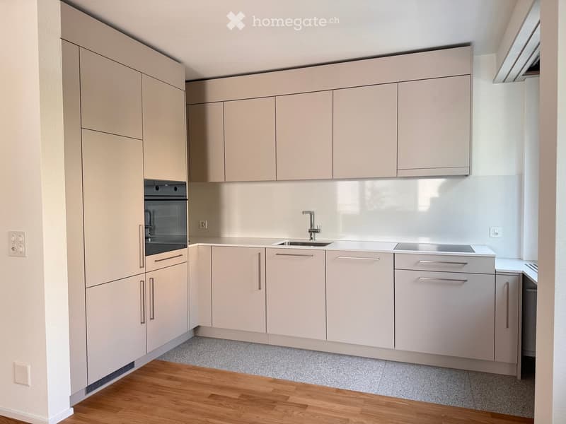 Modern kitchen with light-colored cabinets, a sink, a faucet, and an oven. The floor is a combination of wood and tile.