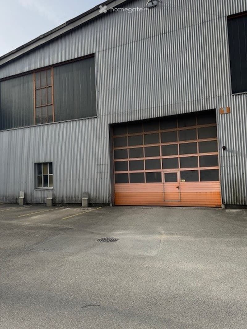 Industrial building with metal siding, large double garage door, windows, parking area