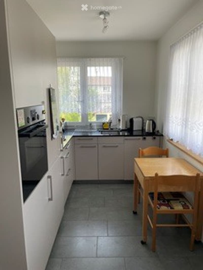 Modern kitchen with white cabinets, grey tiles, and a small wooden dining table with chairs.