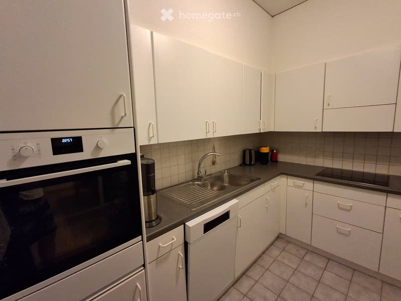 Modern kitchen with white cabinets, stainless steel sink, oven, dishwasher, and countertop items.