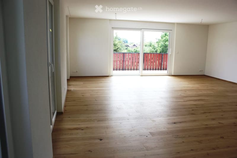 Empty room with wooden flooring, white walls, and large sliding glass doors leading to a balcony area.
