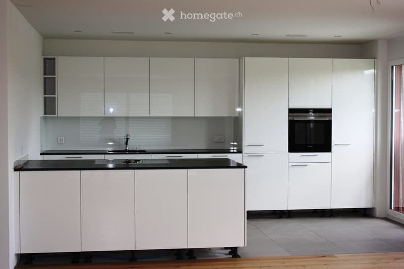 Modern kitchen with white cabinets, black countertops, and built-in appliances including a sink and oven.