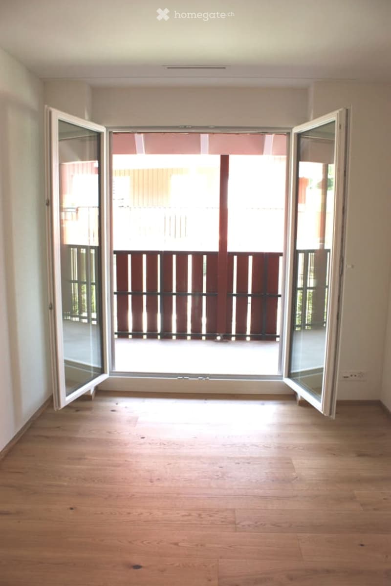 Empty room with wooden flooring, large open sliding doors leading to a balcony with a wooden railing.