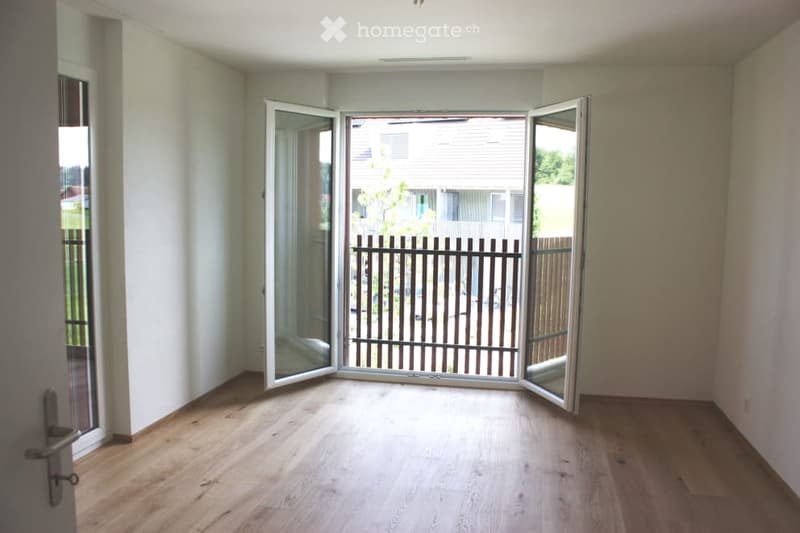 Empty room with wooden flooring, large glass doors leading to an outdoor area, and white walls.
