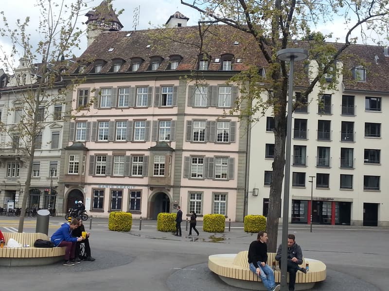 Exterior of building with several windows and arched doorway, yellow flowers in front, people sitting outside