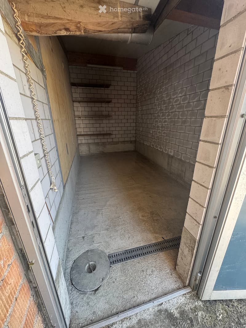 Empty room with concrete floor, tiled walls, and a metal drain cover in the center.