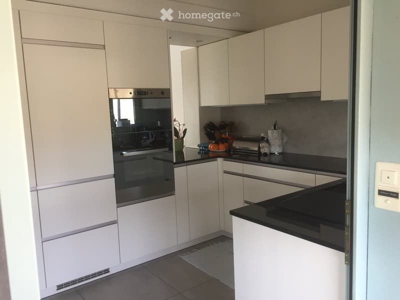 Modern kitchen with white cabinets, black countertops, stainless steel oven, and various kitchen items on the counter.