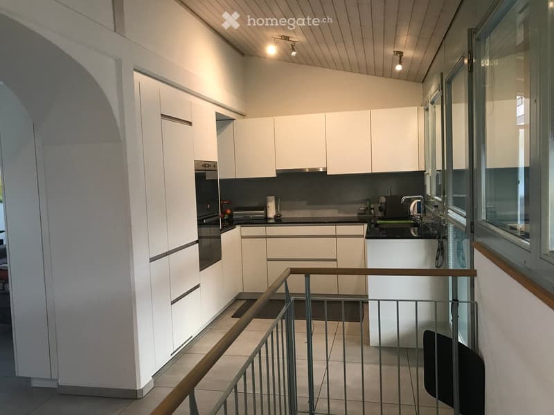 Modern kitchen with white cabinets, stainless steel appliances, and a black countertop. Features a sink with a modern faucet, an oven, and a small balcony area visible through a glass door.