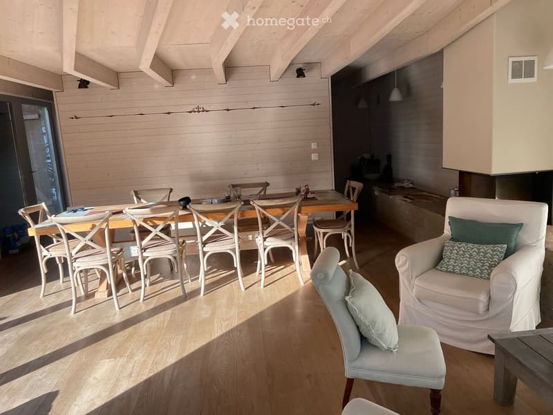 Bright, airy room with wooden floors and white walls, featuring a sofa, chairs, a dining table, and a small bar area.