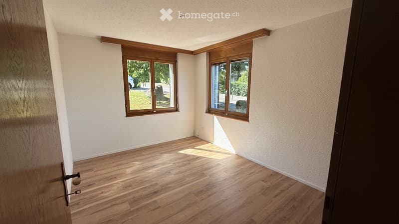 Empty room with wooden flooring, white walls, and two windows with wooden frames. Natural light streams in, illuminating the space.