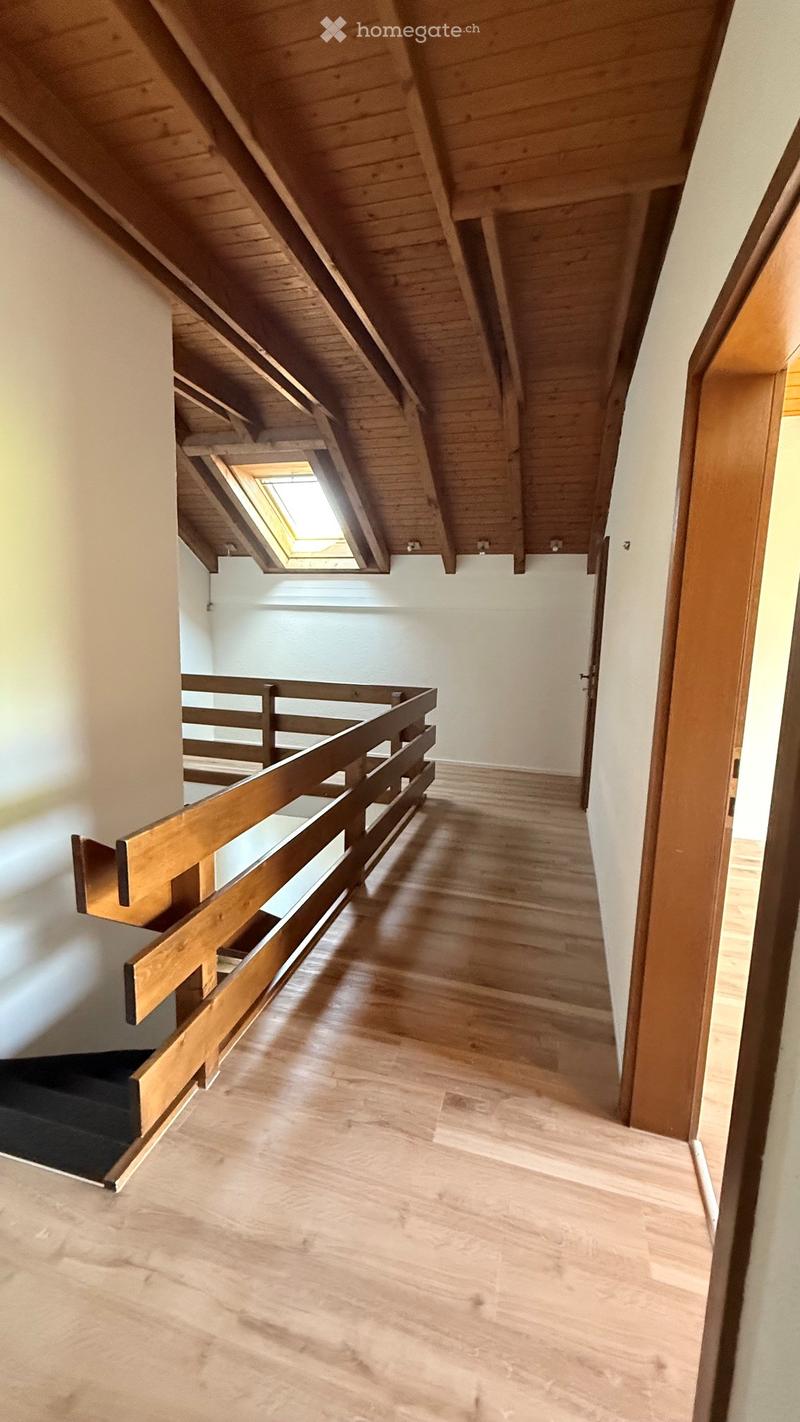 Spacious hallway with wooden flooring, white walls, and a wooden railing leading to an upper level. Features a skylight window and a staircase with a dark carpeted step.