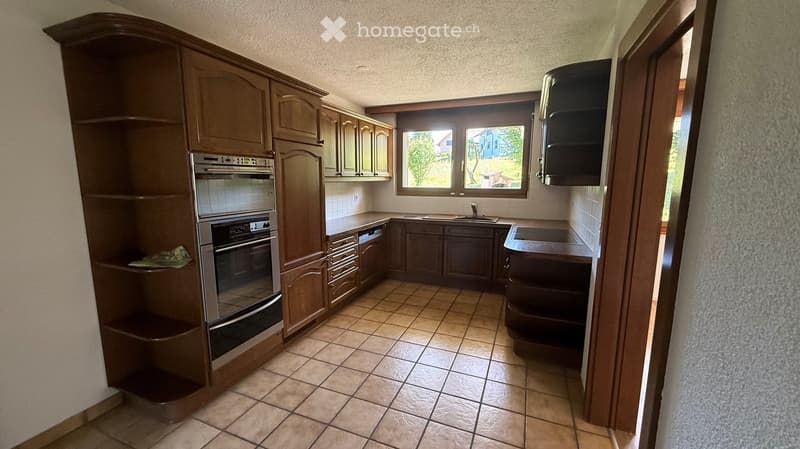 A well-lit kitchen with wooden cabinets, a stainless steel oven, a sink with a faucet, and tiled flooring.