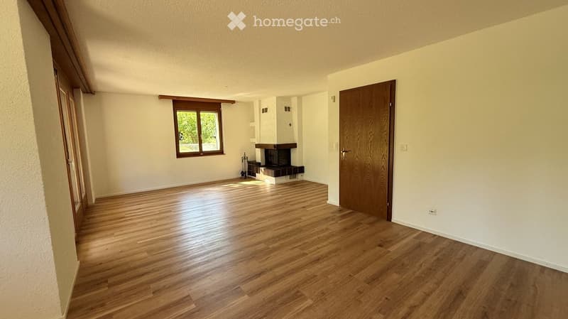 Empty room with wooden flooring, white walls, a fireplace, and a window with wooden frame. No furniture or equipment present.
