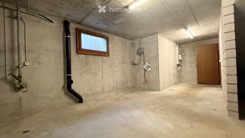 Empty basement space with concrete walls and floor, a small window, a wooden door, and visible pipes and electrical fixtures.