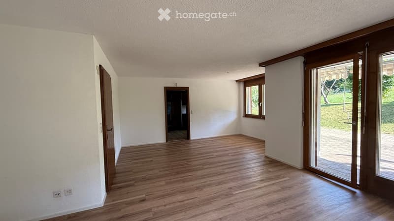Empty room with wooden flooring, white walls, and large windows. Features a sliding glass door leading to an outdoor area.