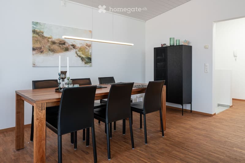 Dining room with a wooden dining table, black chairs, a tall cabinet, and a modern pendant light.