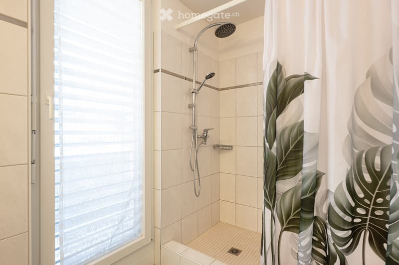 Modern bathroom with a glass-enclosed shower, a sleek showerhead, and a leafy green shower curtain.