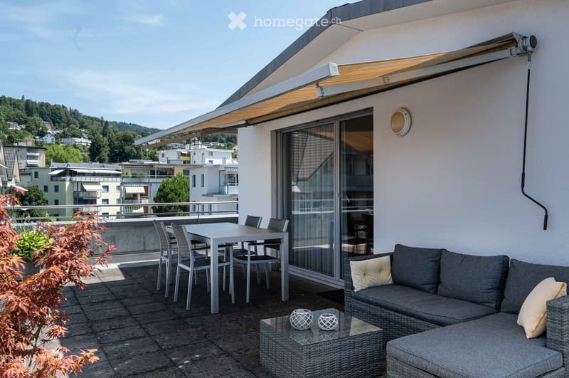 Balcony with a grey wicker sofa, coffee table, dining table with chairs, and a view of the city.