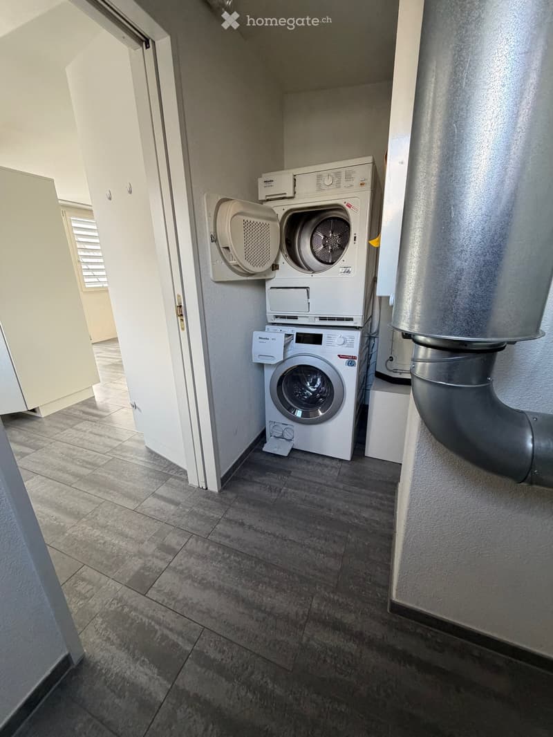 a room with a stacked washing machine and dryer, and tiled flooring