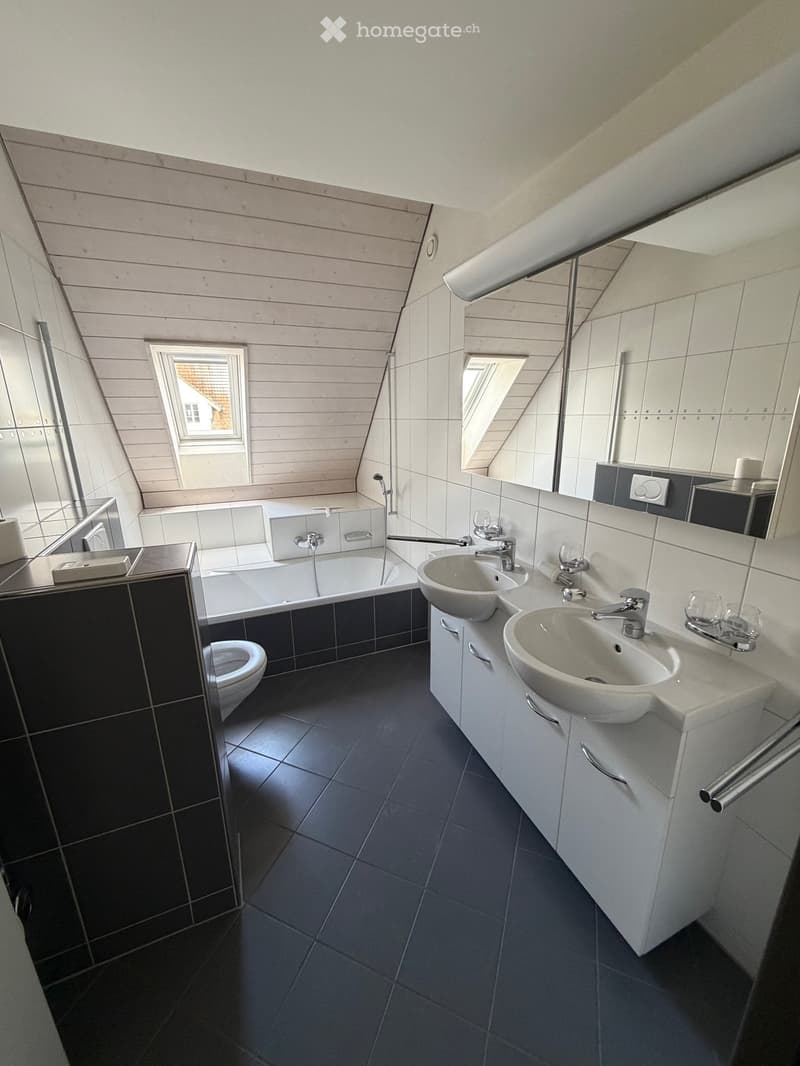 Modern bathroom with bathtub, two sinks, and a toilet.