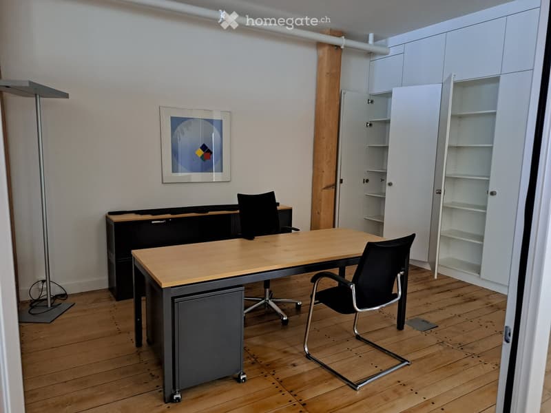 Office space with wooden floor, large wooden desk, two black chairs, white cabinet, and a picture frame on the wall.