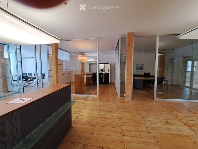 Modern office space with wooden floors, glass partitions, reception desk, chairs, tables, and office furniture.