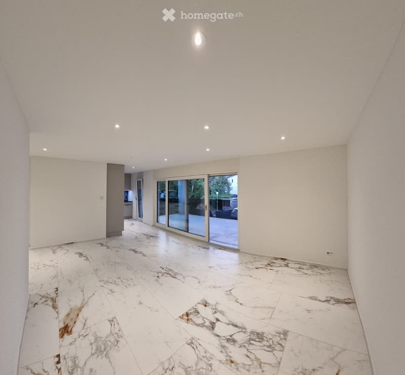 Empty room with white marble flooring, white walls, recessed lighting, and large glass sliding doors leading outside.