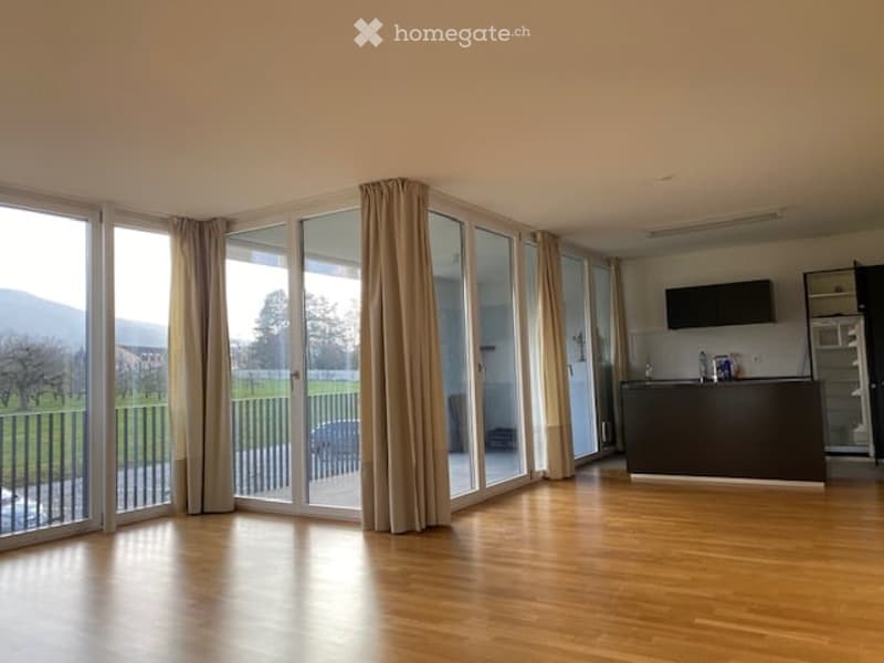 Open-plan living and kitchen area with wooden flooring, large glass sliding doors leading to a balcony with a scenic view, kitchen island, and modern appliances.