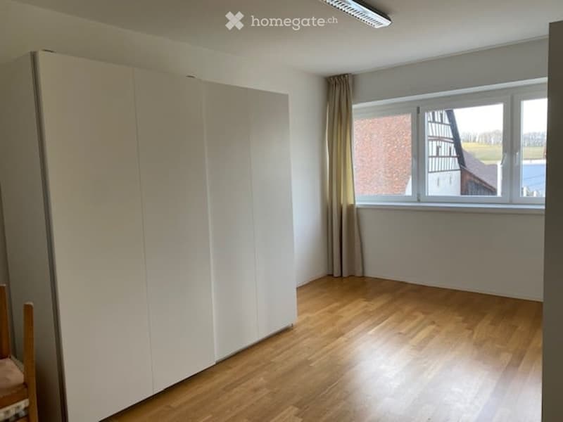 Empty room with wooden flooring, white walls, large window with curtains, and a built-in wardrobe.