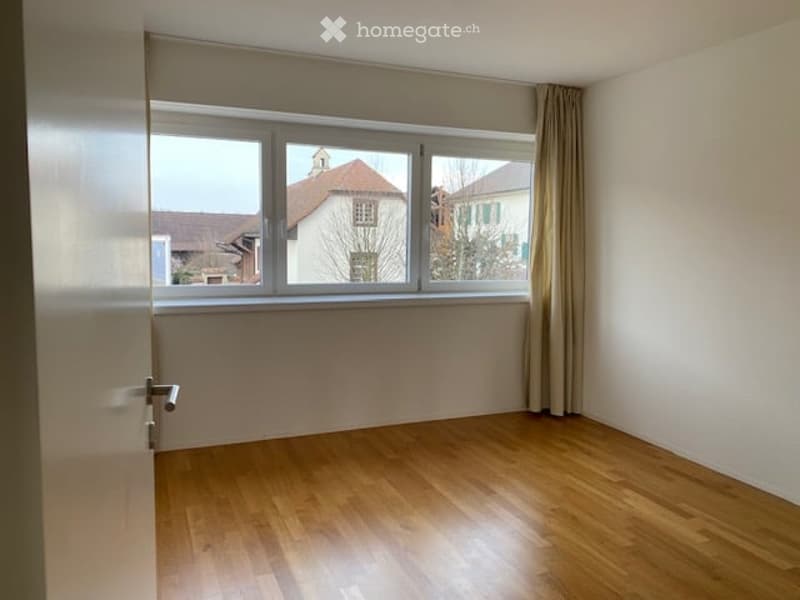 Empty room with wooden flooring, large window with curtains, and a door.