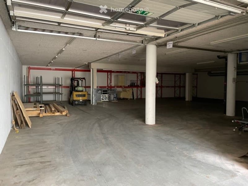 Empty garage with concrete floor, exposed ceiling beams, and a forklift in the background.