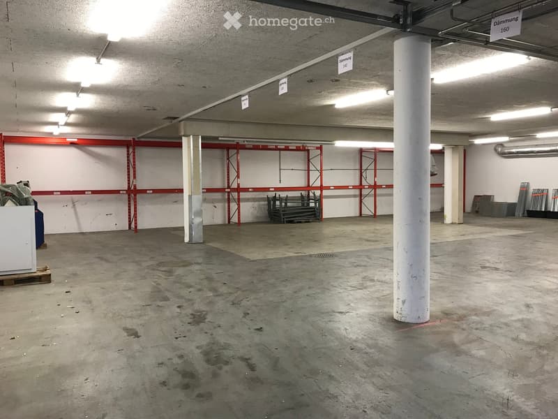 Empty underground parking space with concrete floor, white pillars, and red metal shelving units against the walls.